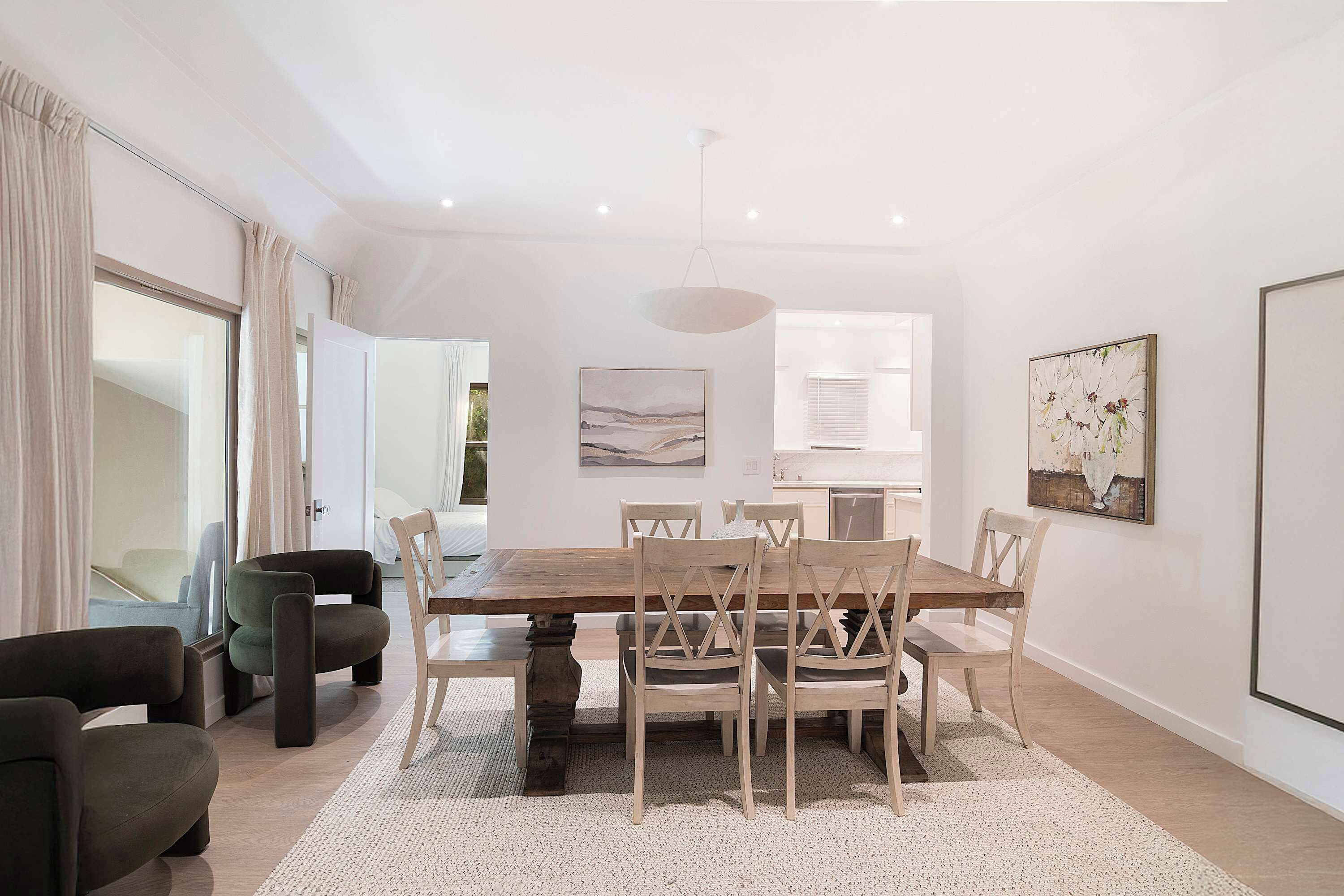 A modern dining area with a wooden table and chairs, a large window with curtains, and artwork on the walls.