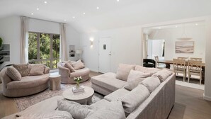 Ein modernes Wohnzimmer mit einem Ecksofa, einem runden Couchtisch und einem Essbereich mit Holztisch und Stühlen.