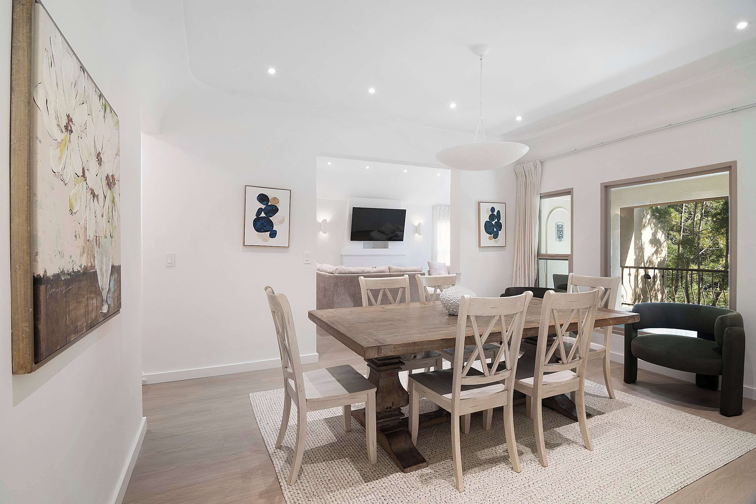A dining area with a wooden table and chairs, a TV mounted on the wall, and artwork on the walls.