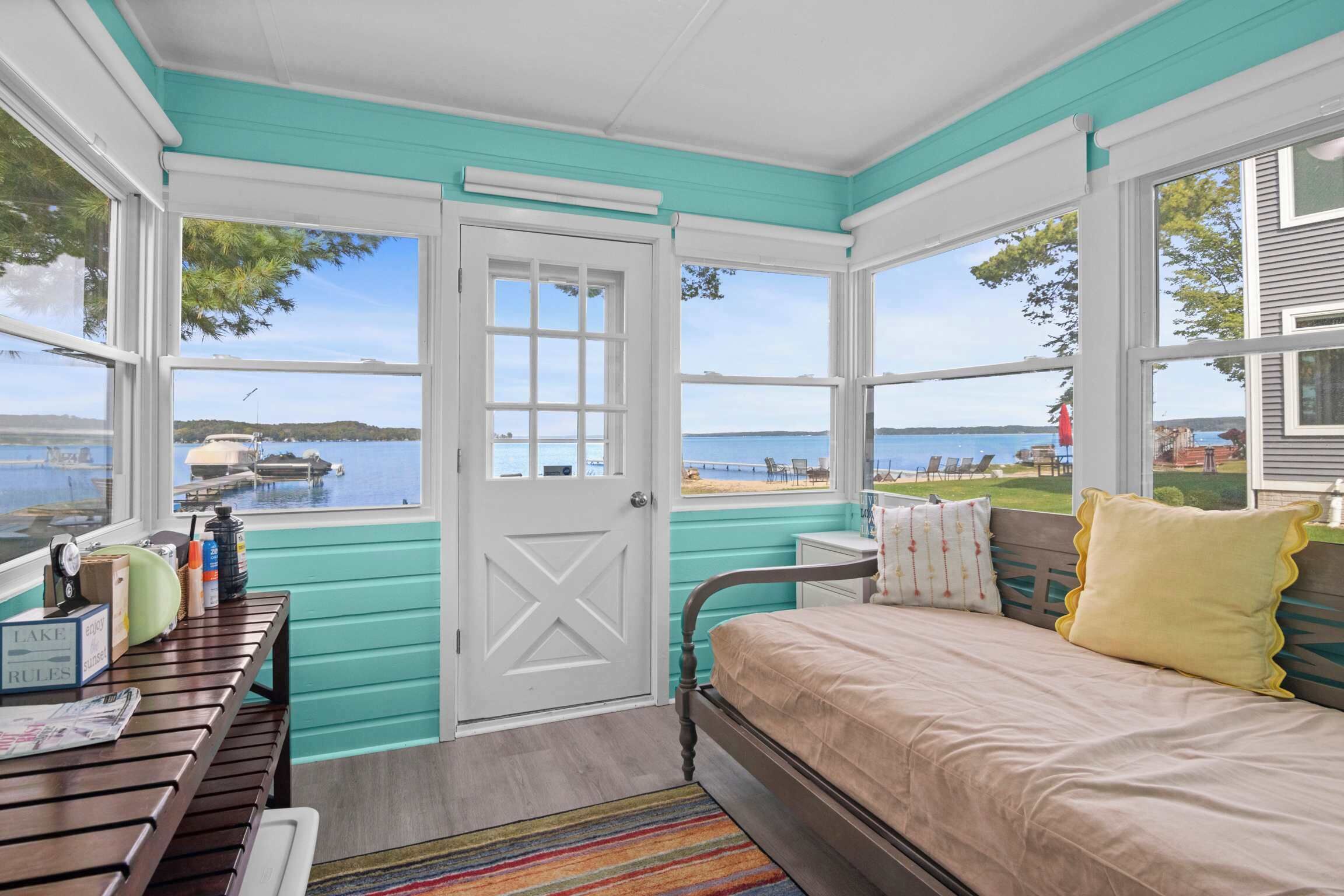 A bedroom with a view of the lake, a wooden bench with items, and a bed with pillows.