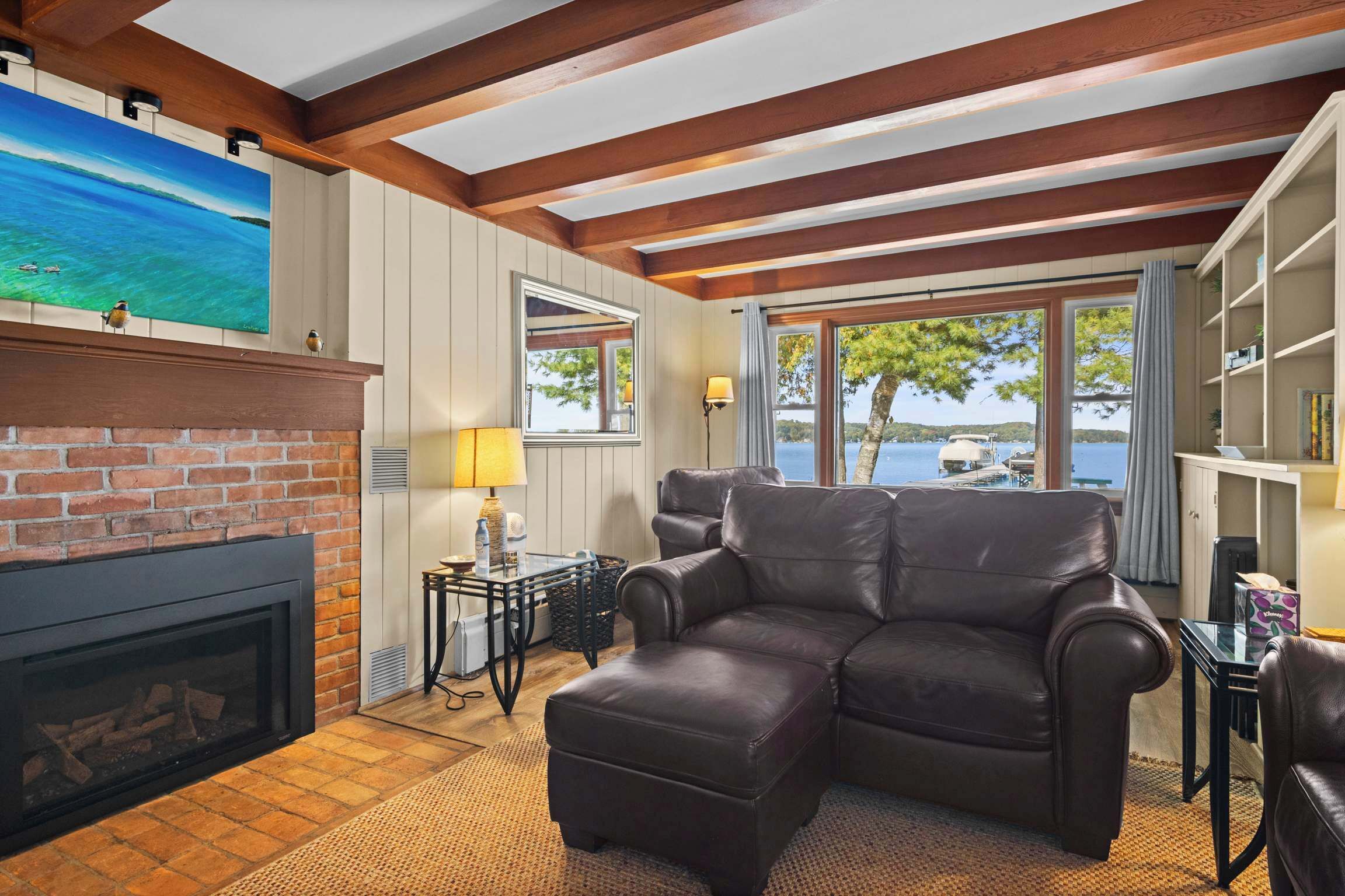 A living room with a fireplace, leather sofa, and a view of the lake.