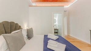 A modern bedroom with a bed, pillows, a blue towel, and a visible bathroom in the background. - Cimabue Mansion (Firenze)