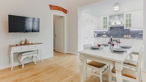 A modern kitchen with white cabinets, a dining table set for four, and a TV mounted on the wall. - Cimabue Mansion (Firenze)