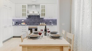 A modern kitchen with white cabinetry, a central island, and a dining area set for a meal. - Cimabue Mansion (Firenze)