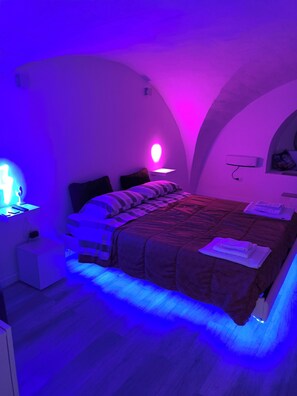 A bedroom with a bed, bedside tables, a wall-mounted lamp, and a shelf with items.