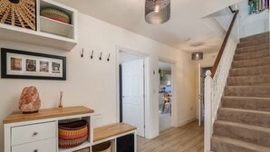 A modern interior with a staircase, a hallway leading to a kitchen, and a white wall with framed pictures. - Pass the Keys | Spacious, Modern Family Home - 20 mins to Oxford (Marcham)