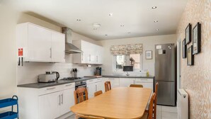 A modern kitchen with white cabinets, a wooden dining table, and a blue cart. - Pass the Keys | Spacious, Modern Family Home - 20 mins to Oxford (Marcham)