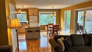 A modern kitchen with a dining area, wooden flooring, and a cozy living room with a sofa. - Riverfront cottage-style home in the heart of the Acadian Peninsula (Pokemouche)