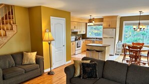 A cozy living room with two sofas and a lamp, a kitchen with wooden cabinets and a dining area with a table and chairs. - Riverfront cottage-style home in the heart of the Acadian Peninsula (Pokemouche)