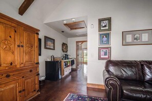 Uma sala de estar ampla com um armário de madeira, um sofá de couro preto e uma cozinha ao fundo.