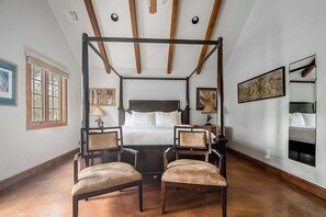 A bedroom with a four-poster bed, two chairs, a nightstand, and a bedside table.