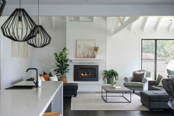 A modern living room with a fireplace, seating area, and a kitchen counter.