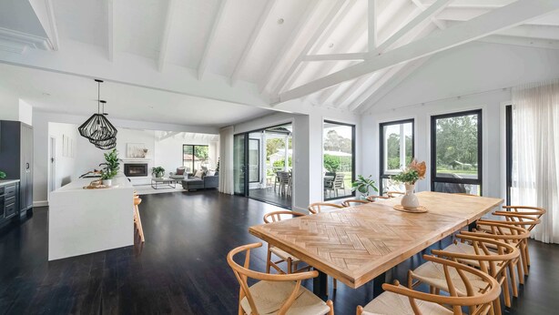 A spacious living area with a large wooden dining table, multiple chairs, and a kitchen in the background. - Homestead on Fennell - Fresh Eggs, Farm & BBQ Fun (Blackalls Park)