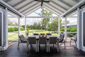 A covered patio with a table and chairs, overlooking a well-maintained lawn and trees.
