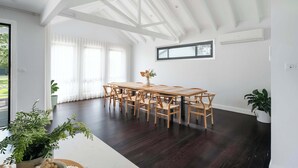 A spacious dining area with a long wooden table and matching chairs, white walls, and a high ceiling with exposed beams. - Homestead on Fennell - Fresh Eggs, Farm & BBQ Fun (Blackalls Park)