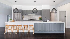 A modern kitchen with a large island, grey cabinets, and three wooden stools. - Homestead on Fennell - Fresh Eggs, Farm & BBQ Fun (Blackalls Park)