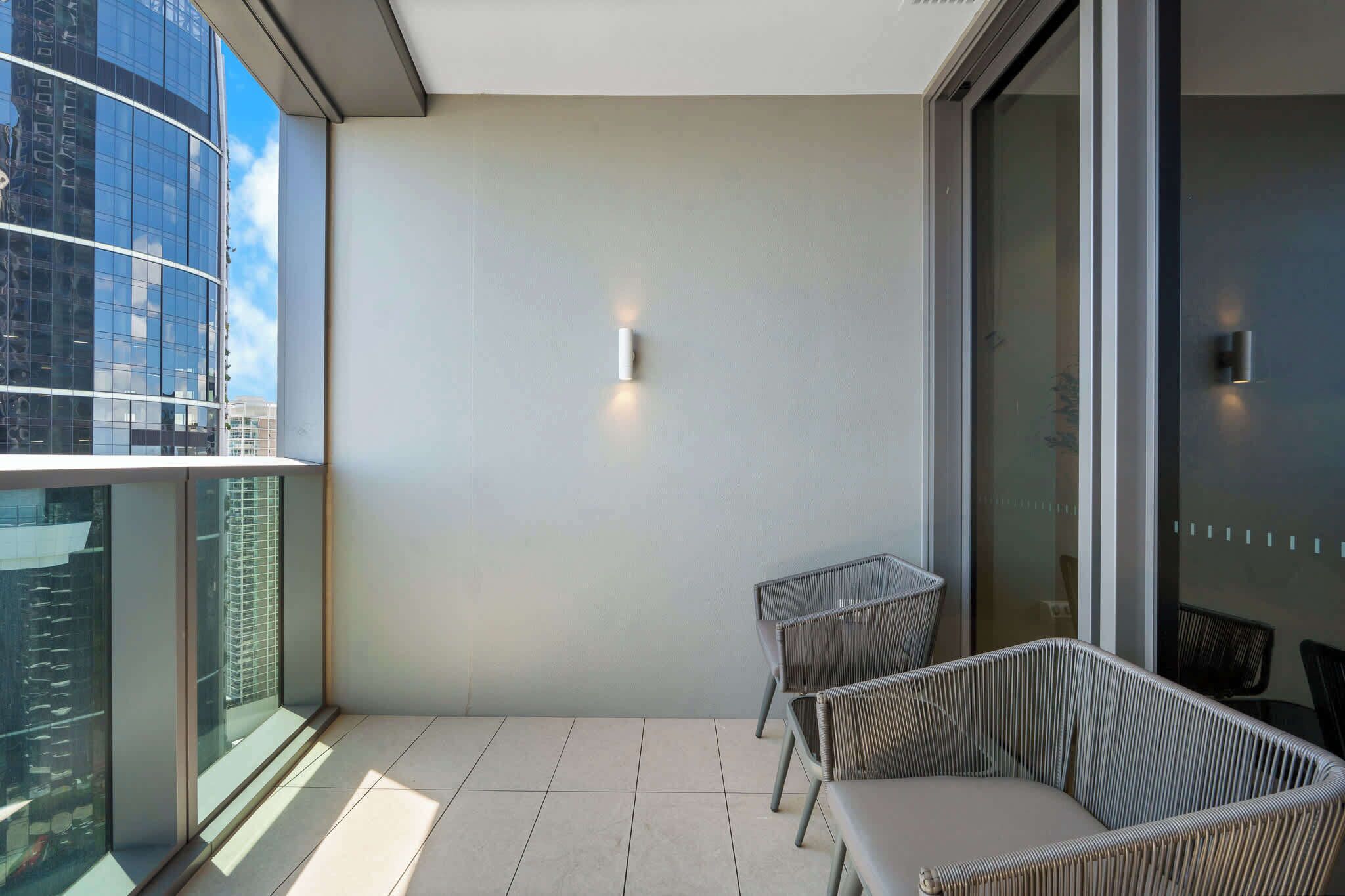 Ein Balkon mit Blick auf ein modernes Gebäude, zwei Korbstühle und eine Glastür.