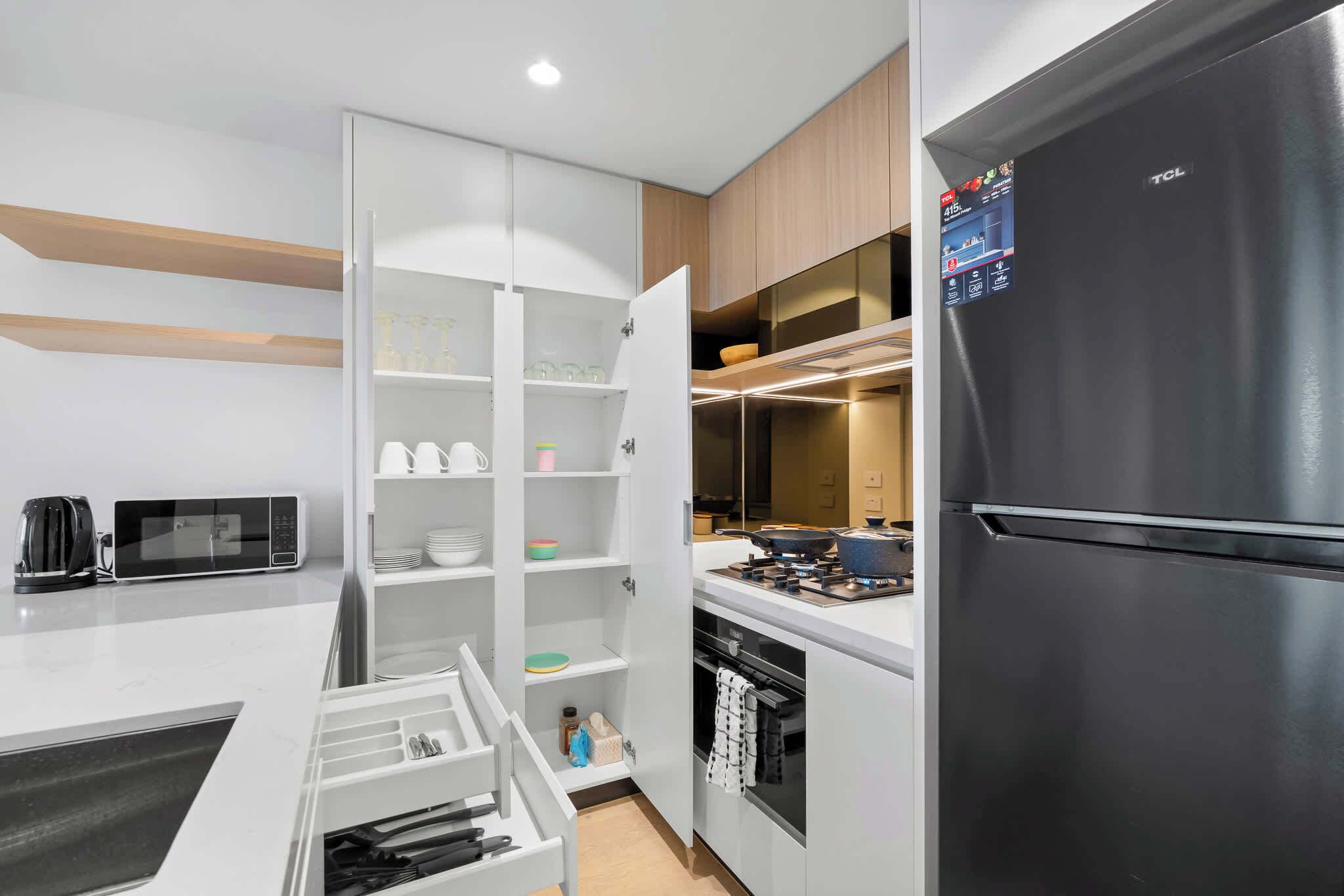 Uma cozinha moderna com geladeira preta, armários brancos e micro-ondas.