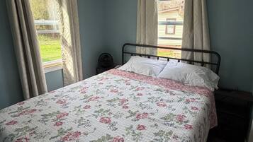 Un dormitorio con cama, dos ventanas con cortinas, un ventilador y vistas al exterior.