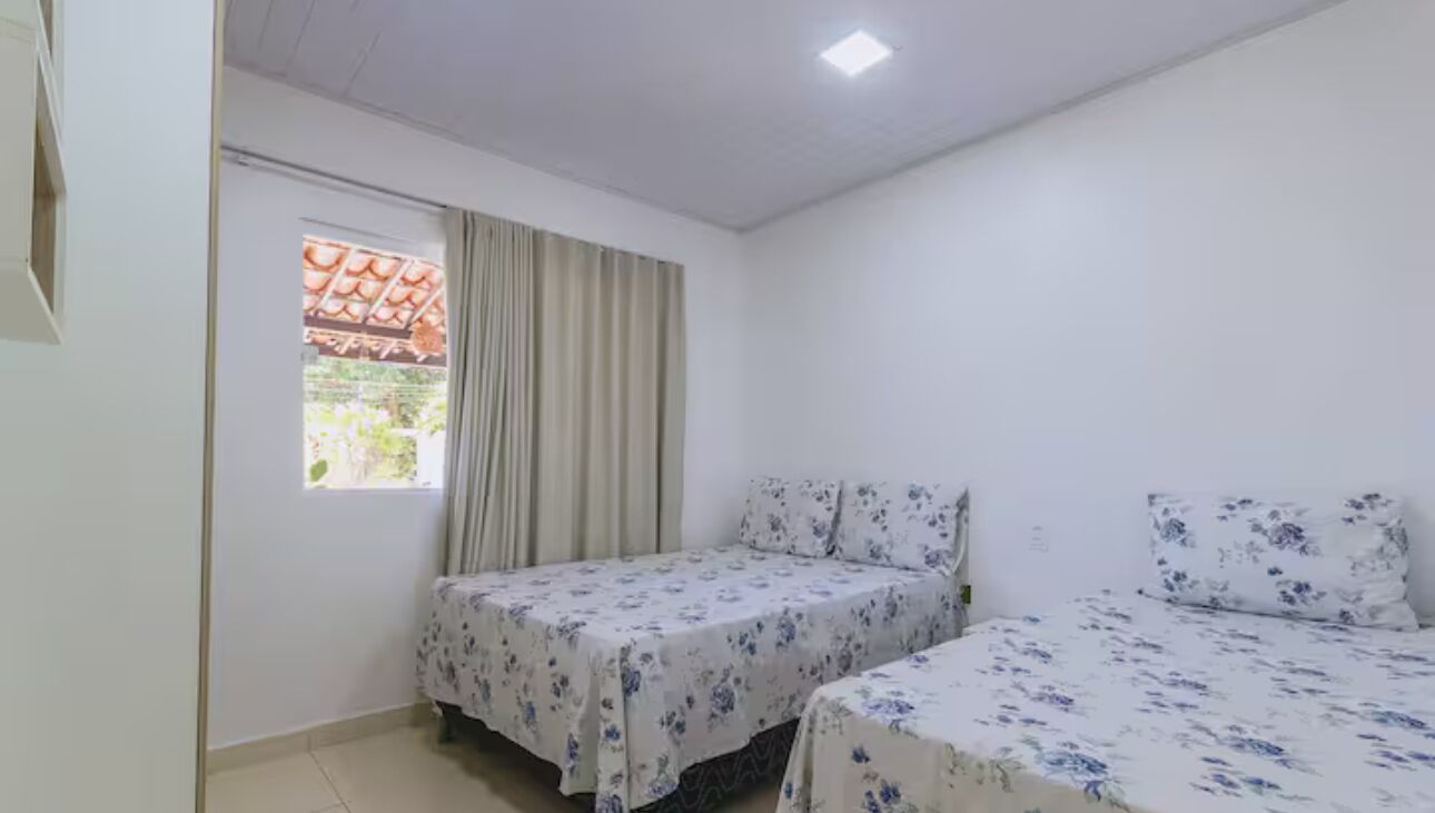 A room with two beds, a window with curtains, and a ceiling light.