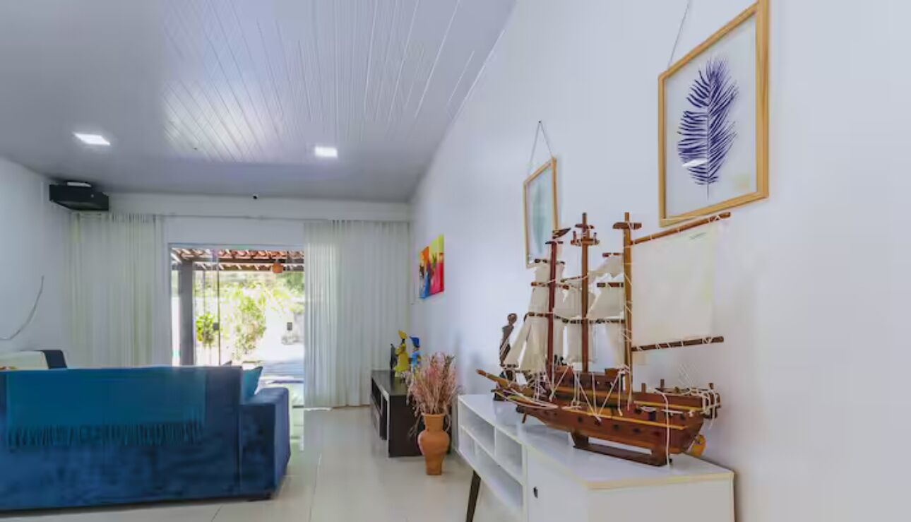 Una sala de estar moderna con un sofá azul, un modelo de barco de madera y un ventanal con cortinas.