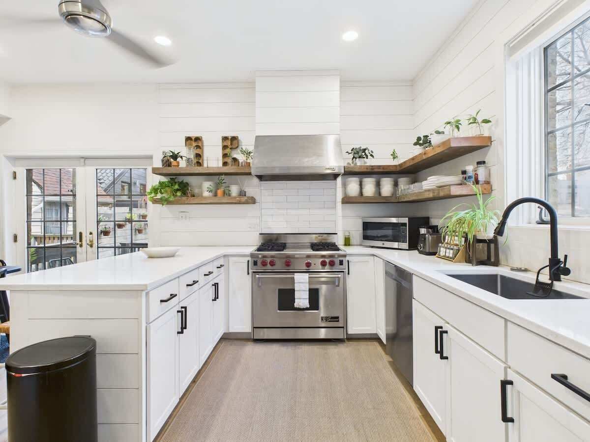 Een moderne keuken met witte kastjes, een roestvrijstalen fornuis en houten planken met planten.