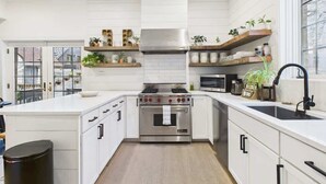 A modern kitchen with white cabinetry, a stainless steel stove, and wooden shelves with plants.