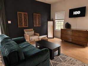 A living room with a dark green sofa, a wooden dresser, and a television displaying the HBO logo.