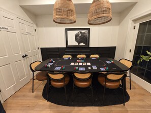 A dining area with a black table set for a game, surrounded by wicker chairs, with a framed animal picture on the wall.