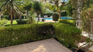 A landscaped garden with a swimming pool, palm trees, and neatly trimmed hedges. - NEW! Spacious two-bedroom apartment. 2 terraces, pool, 10 minutes to the beach. (Lote 78, Bloco D.)