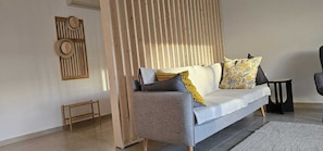 A modern living room with a grey sofa, wooden slat partition, and a small wooden stool.