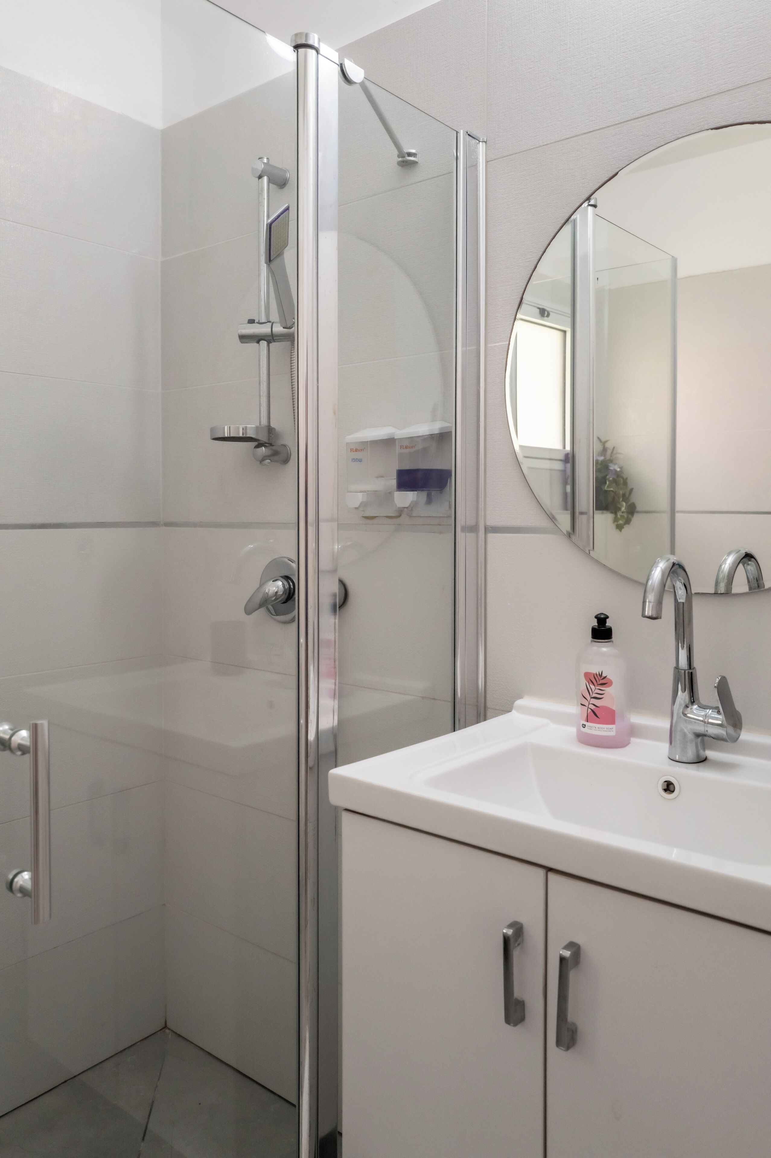 A modern bathroom with a glass shower enclosure, a white sink with a mirror, and a cabinet with handles.