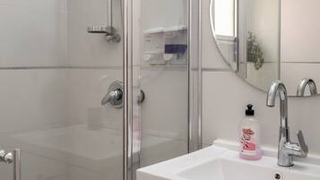 A modern bathroom with a glass shower enclosure, a white sink with a mirror, and a cabinet with handles.