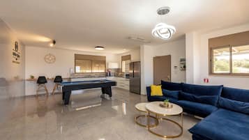 A modern living room with a pool table, a blue sofa, and a round coffee table.