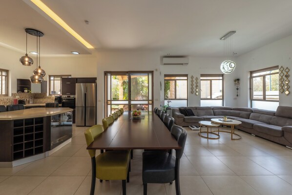Amplia sala de estar con una larga mesa de comedor, un sofá y una cocina equipada con electrodomésticos modernos.