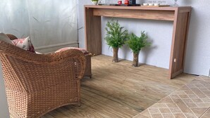A room with a wicker sofa, a wooden console table with decorative items, and a tiled floor. - Pousada da Nega (Picarras)