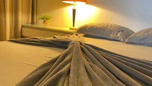 A neatly made bed with a grey blanket, a bedside lamp, and a small plant on the nightstand. - Pousada da Nega (Picarras)