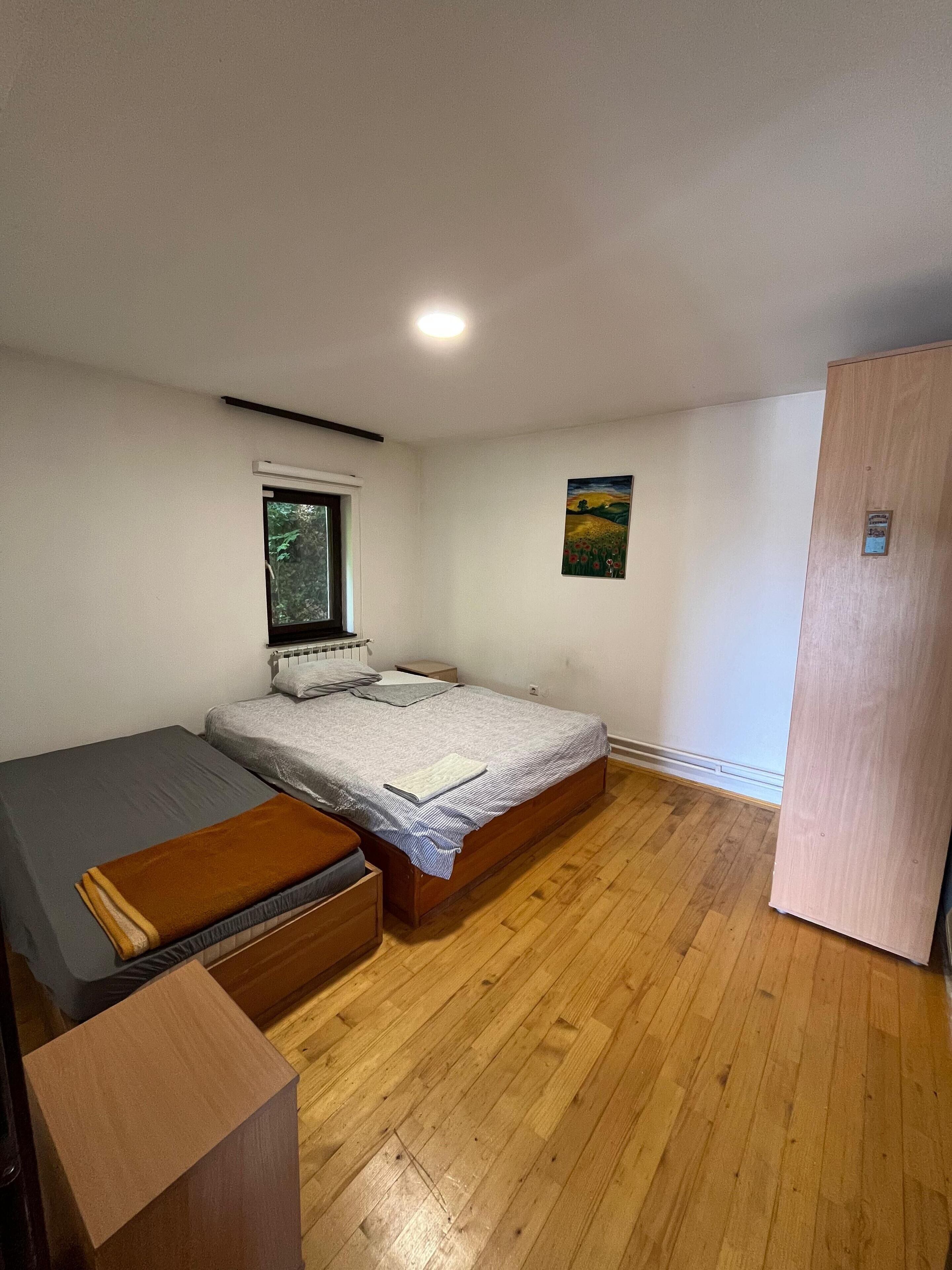 A bedroom with a bed, a window, a painting, and a wooden floor.