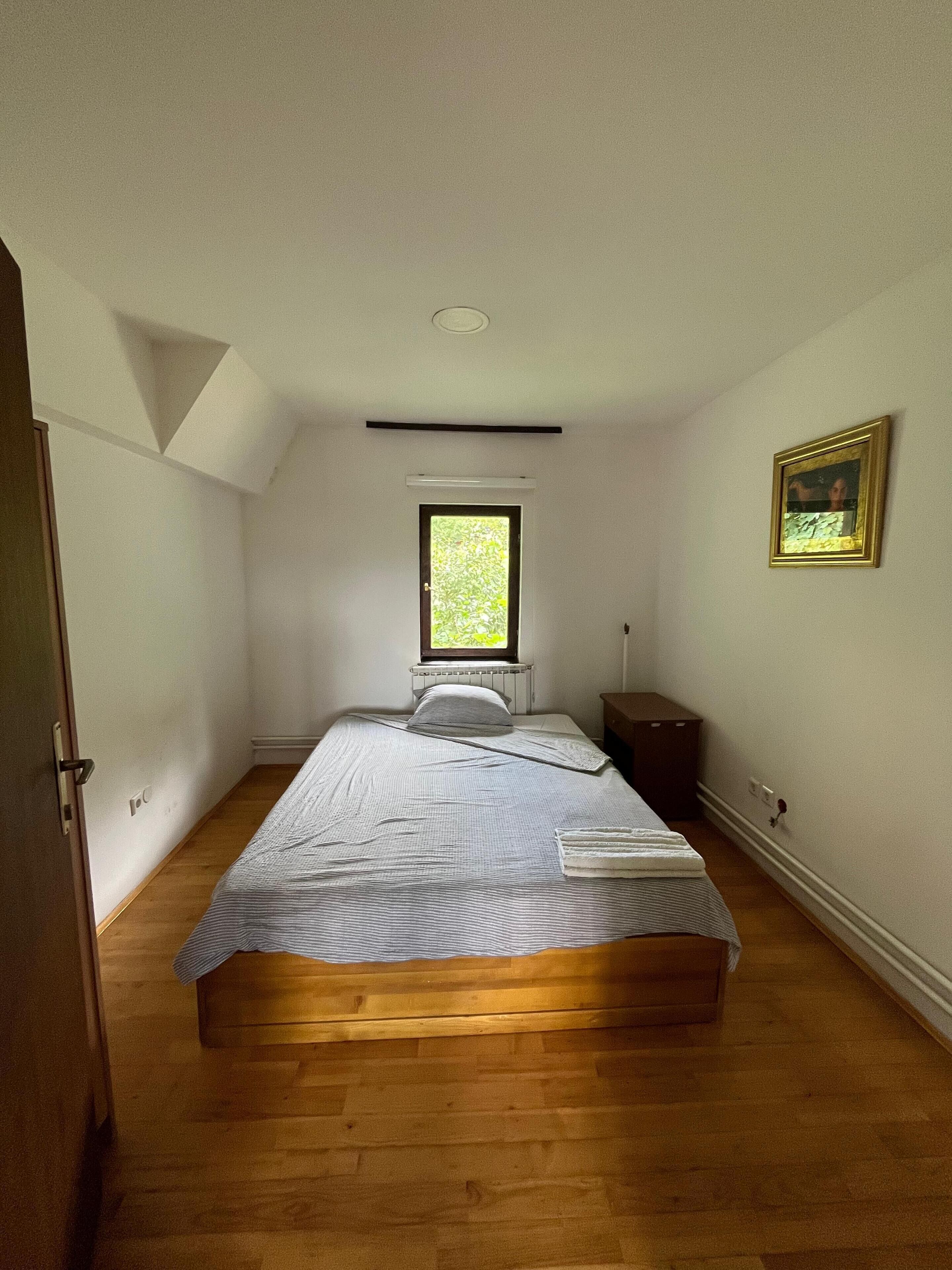 Ein Schlafzimmer mit einem Einzelbett, einem Fenster, einem Heizkörper, einem Nachttisch und einem gerahmten Bild an der Wand.