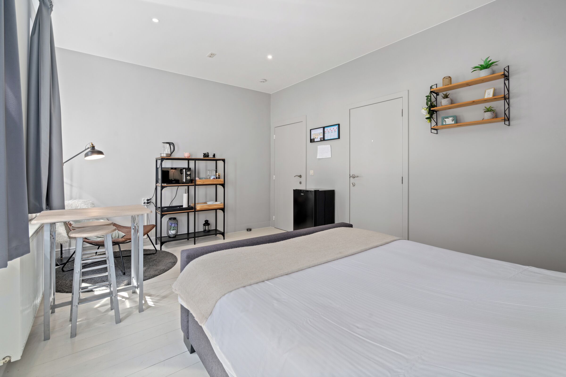 Une chambre moderne avec un grand lit, un bureau avec une chaise, une armoire et une étagère avec des plantes.