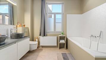 Une salle de bain équipée d’une baignoire, de toilettes, d’un lavabo et d’une fenêtre avec des rideaux.