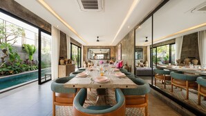 A dining area with a long table set for a meal, surrounded by chairs, and a view of a swimming pool.