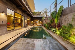 A modern building with a swimming pool, outdoor seating, and lush greenery.