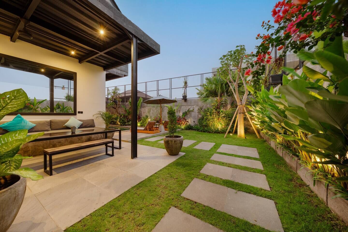 Een modern terras buiten met een bank, een bijzettafeltje en een grote plantenbak.