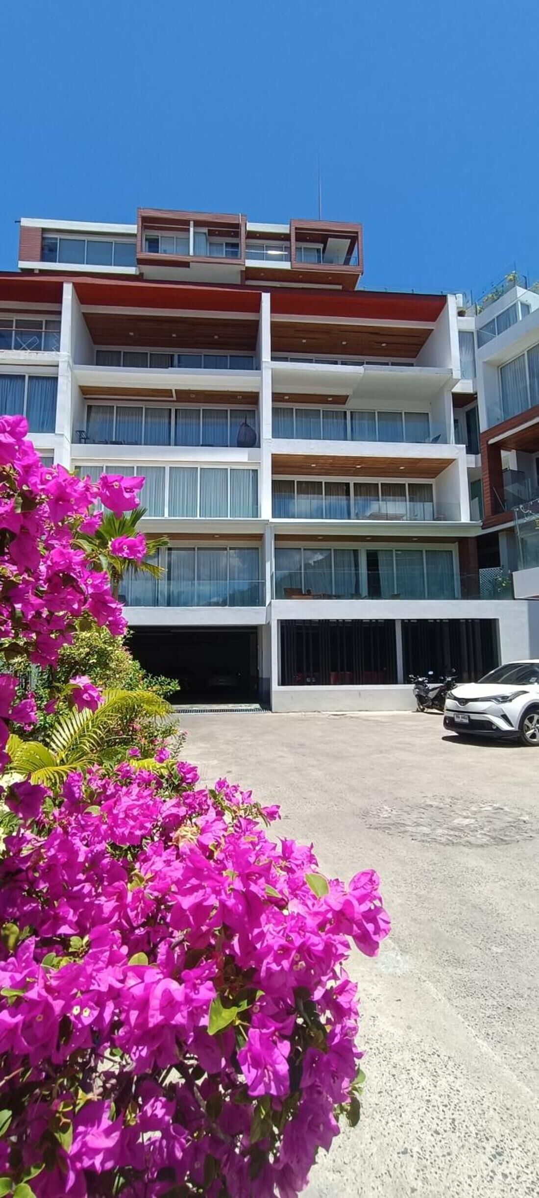 A multi-story hotel with balconies, large windows, and a parking area.