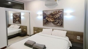 A modern hotel room with a large bed, a mirror, a wall-mounted air conditioner, and a large floral painting.