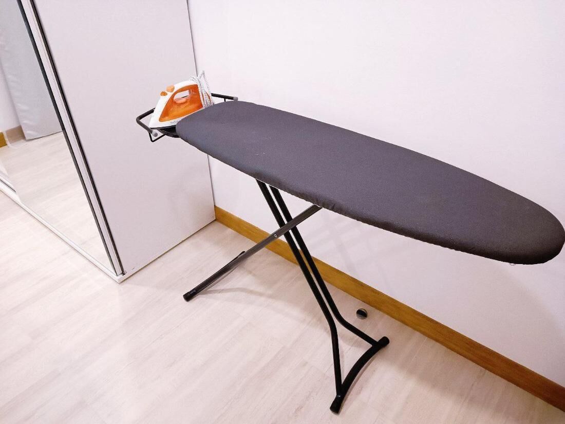 A portable ironing board with a built-in iron, placed against a wall in a room with a wooden floor.