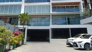 A multi-story building with a modern architectural design, featuring a central entrance and a parking area with a white car.