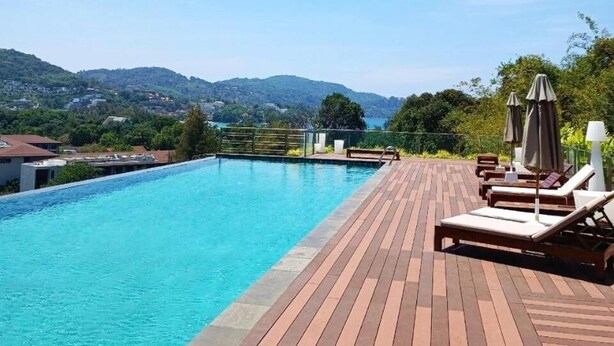 A swimming pool with a wooden deck, lounge chairs, and umbrellas.