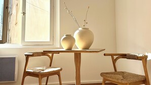 Una habitación con una mesa redonda de madera, dos sillas de mimbre y dos jarrones de cerámica con flores secas en el alféizar.